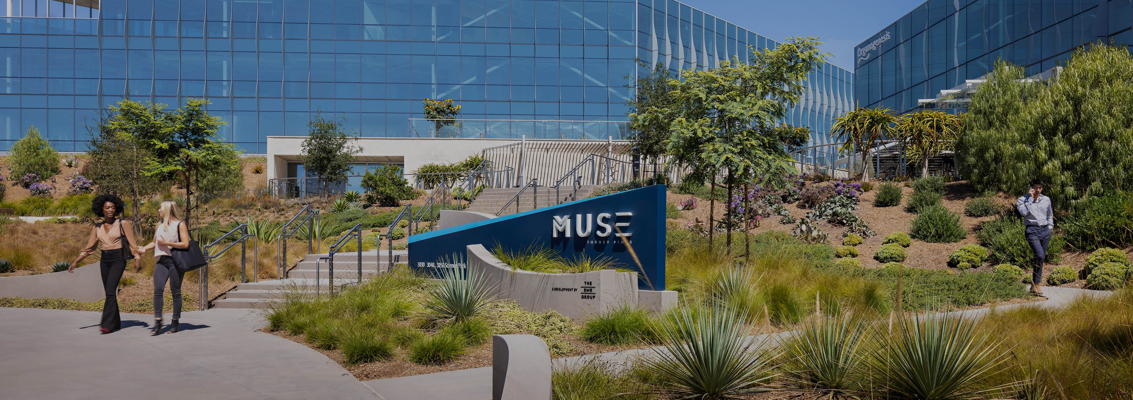 The entrance to the Muse at Torrey Pines property at 3030 Science Park in San Diego, California with the Muse sign, native landscaping, and two glass covered buildings. The buildings are owned by DHC and are LEED Silver Certified